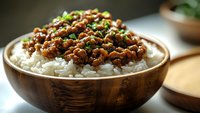 Savory minced meat with soy sauce and spices served over steamed white rice in wooden bowl, garnished with fresh chopped green onions, Asian cuisine style.