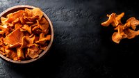 Fresh wild chanterelle mushrooms in wooden bowl on dark concrete background, raw organic forest fungi, top view with copy space for menu design.