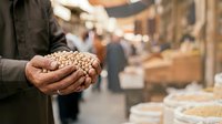 Farmer holding handful of chickpeas at market stall with blurred background, showcasing fresh legumes for agricultural and food industry use.