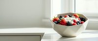 Fresh mixed berries including strawberries, blueberries and raspberries in a white ceramic bowl on a bright kitchen counter with natural light.