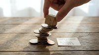 Male hand of African descent placing wooden cube on top of stacked coins on wooden surface next to inflation rising text card for financial growth and economic concepts.