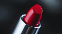 Vibrant red lipstick in metallic silver case against dark background, macro photography showing texture and glossy finish of luxury cosmetic product.