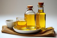 Glass bottles with golden oil and small glass on white ceramic plate with brown napkin. Natural cooking ingredients for healthy Mediterranean cuisine.