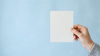 Hand holding blank white card against light blue background for mockup and branding purposes.