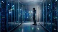 Professional IT specialist standing in modern data center corridor surrounded by server racks with blue LED lights for technology infrastructure.