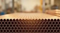 Copper pipes stacked in industrial warehouse with warm lighting creating depth of field effect for construction and plumbing industry applications.