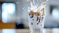 Milk splash with coffee in transparent glass creating dynamic motion effect. Frozen moment of liquid collision with dark roasted coffee beans and drops.