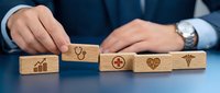Healthcare professional in business attire arranging wooden blocks with medical and financial icons, symbolizing health insurance, medical costs, and wellness planning for commercial use.