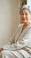 Senior Asian woman with gray hair wearing beige cardigan, smiling warmly while sitting indoors. Suitable for healthcare, wellness, lifestyle and aging gracefully concepts.