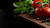 Fresh red tomatoes with water drops and aromatic herbs on dark wooden cutting board against black background, macro food photography with copy space.