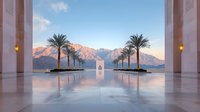 Serene architectural view with palm trees and mountains at sunset, featuring symmetrical columns, reflective marble floor and minimalist design elements.