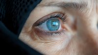 Close up macro shot of bright blue eye with natural eyelashes and skin texture details, showing fine wrinkles and pores in dramatic lighting for medical or beauty concepts.
