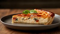 Savory quiche slice with eggs, cheese and vegetables on dark plate, garnished with fresh basil leaf for breakfast, brunch or lunch meal preparation.