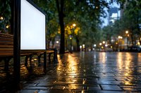 Empty white billboard in rainy evening park with wet cobblestone path, wooden bench and glowing street lights creating atmospheric urban scene.
