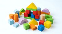 Colorful wooden building blocks set with geometric shapes including cubes, cylinders, triangles and arches scattered on white background for educational play.