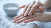 Woman applying moisturizer cream on hands with bowl in background for skincare routine and beauty treatment at spa.