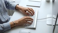 Professional woman hands typing on white laptop keyboard at modern office desk workspace for business productivity and remote work.