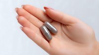 Female hand with manicured nails holding two silver metallic capsules or pills against light background, medical and healthcare concept for supplements or medication.