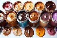 Colorful collection of nut butters and chocolate spreads in glass jars with swirled textures, arranged in rows showing variety of natural and flavored options.