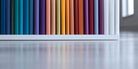 Colorful row of books arranged by spectrum colors on white shelf creating rainbow gradient effect with soft reflection on glossy surface. Modern minimalist design.