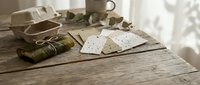 Vintage military dog tags and camouflage cap on weathered wooden table with soft natural lighting creating nostalgic wartime atmosphere for memorial designs.