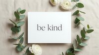 Be kind motivational quote card surrounded by eucalyptus branches and white ranunculus flowers on linen background.