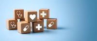 Wooden blocks with medical healthcare symbols including stethoscope, heart, cross and pill icons arranged on blue background for wellness concepts.