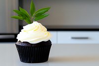 Dark chocolate cupcake with creamy vanilla frosting swirl and fresh green leaves garnish on white counter, elegant dessert presentation in modern kitchen.