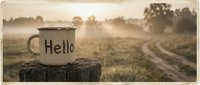Vintage enamel mug with Hello inscription on rustic wooden stump, misty morning countryside landscape with golden sunrise light.
