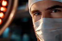 Close-up portrait of male medical professional wearing surgical mask with intense blue eyes in operating room with surgical lights creating dramatic atmosphere.