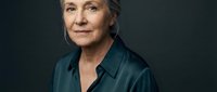 Confident mature Caucasian businesswoman in dark green silk shirt against gray background. Professional portrait for corporate branding and leadership concepts.