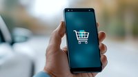 Shopping cart icon on smartphone screen held by hand against blurred background, representing mobile commerce and online shopping application for retail business.