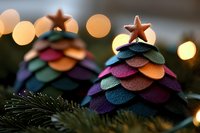 Colorful felt Christmas trees with layered scalloped circles in rainbow colors topped with copper stars, against blurred bokeh lights and evergreen branches.