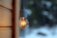 Glowing vintage LED filament bulb hanging against blurred winter background, warm light illuminating wooden wall surface, creating cozy atmosphere.