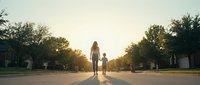 Young woman walking down empty suburban street at golden hour sunset with trees and houses creating peaceful neighborhood atmosphere for lifestyle content.