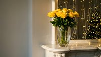 Yellow roses in crystal vase on white mantel with warm fairy lights creating cozy home decor atmosphere for romantic interior design and floral arrangements.