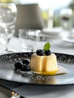 Elegant vanilla panna cotta dessert topped with fresh blueberries and mint on black plate. Gourmet restaurant presentation for fine dining menu photography.