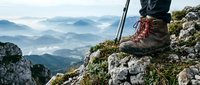 Hiker boots on rocky mountain summit with trekking pole and misty valley landscape below. Adventure outdoor recreation concept for active lifestyle exploration.