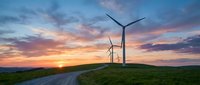 Wind turbines on green hills at sunset with dramatic colorful sky and winding path. Renewable energy concept for sustainable power generation and eco-friendly technology.