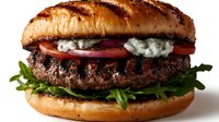 Grilled beef burger with blue cheese, fresh tomatoes, and arugula on toasted brioche bun against dark background, close up view of gourmet hamburger.