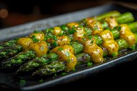 Fresh green asparagus spears topped with melted butter sauce and herbs served on dark plate, close up view of gourmet vegetable appetizer in restaurant setting.