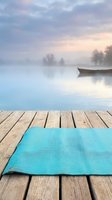 Yoga mat on wooden dock overlooking misty lake with boat and trees at dawn, suitable for wellness, fitness, meditation, and lifestyle design projects.