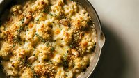 Creamy baked cauliflower gratin with golden cheese crust and fresh herbs in cast iron skillet, comfort food casserole ready to serve for family dinner.