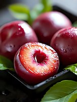 Fresh ripe plums with water drops on dark background, cut plum showing juicy red flesh and bright center, surrounded by green leaves, macro shot.