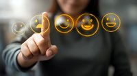 Hand pointing at glowing yellow emoji faces showing different expressions of happiness and satisfaction on dark background, concept of customer feedback.