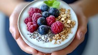 Healthy breakfast bowl with fresh berries, granola and chia seeds held in hands. Nutritious morning meal with raspberries, blueberries and oats for wellness.