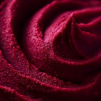 Vibrant red velvet frosting swirls in extreme macro detail showing rich texture and deep burgundy color tones, creating an abstract pattern of curves and shadows.