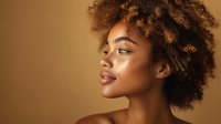 Young African American woman with natural curly afro hair and glowing skin against warm golden background, side profile portrait showing confident expression.