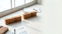 Wooden blocks showing year transition from 2026 to 2027 on white desk with business documents and charts for planning concept.