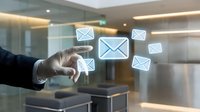 Businessman in formal attire touching digital mail envelope icon among floating message symbols in modern office environment, representing email communication and digital messaging technology.